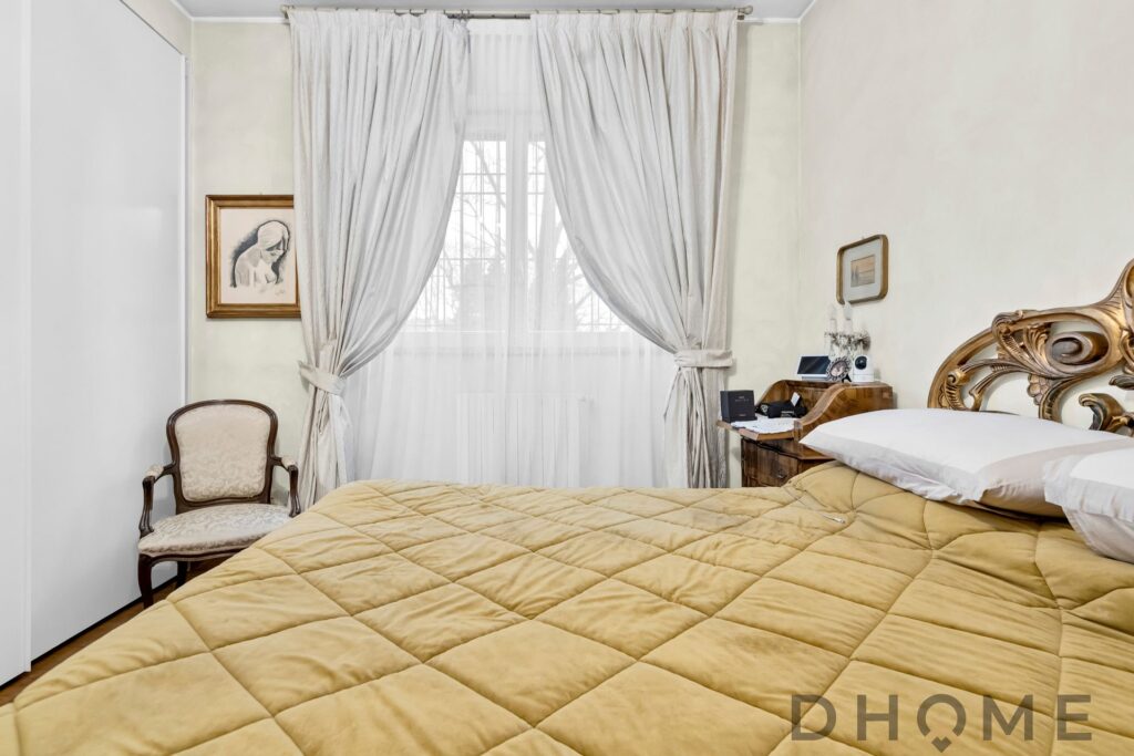 Letto matrimoniale con testiera in legno laccato e copriletto beige, raggio di sole naturale dalla finestra.