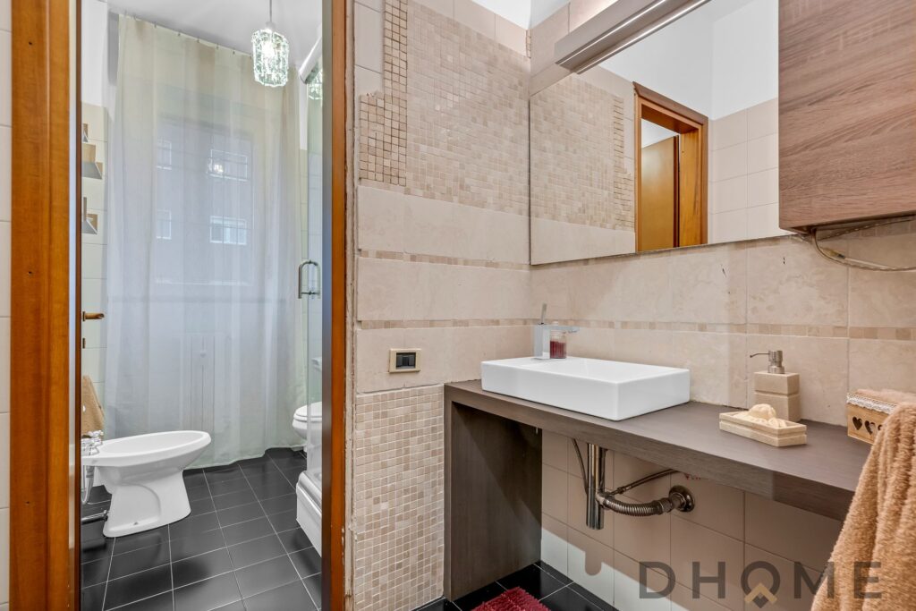 Lavabo moderno in bagno con rivestimenti beige e dettaglio mosaico, caratterizzato da stile elegante e funzionale.