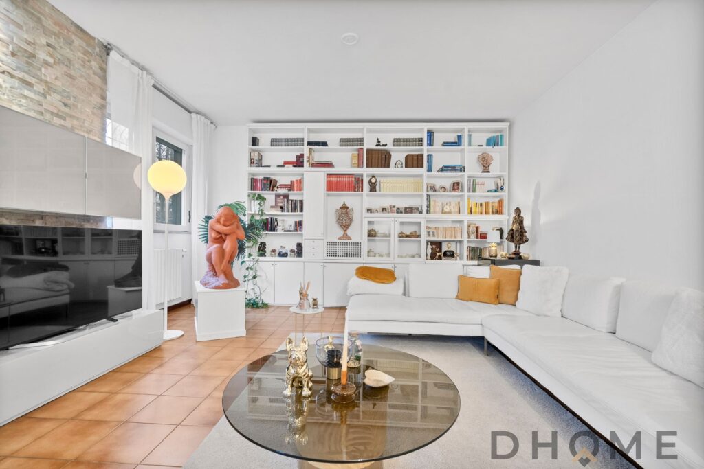 Soggiorno moderno con libreria bianca, divano angolare e decorazioni artistiche.