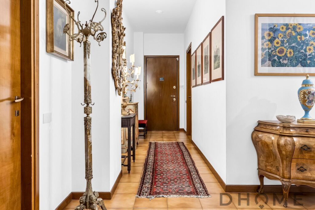 Corridoio di casa decorato con arredamento classico, quadri e lampadario moderno.