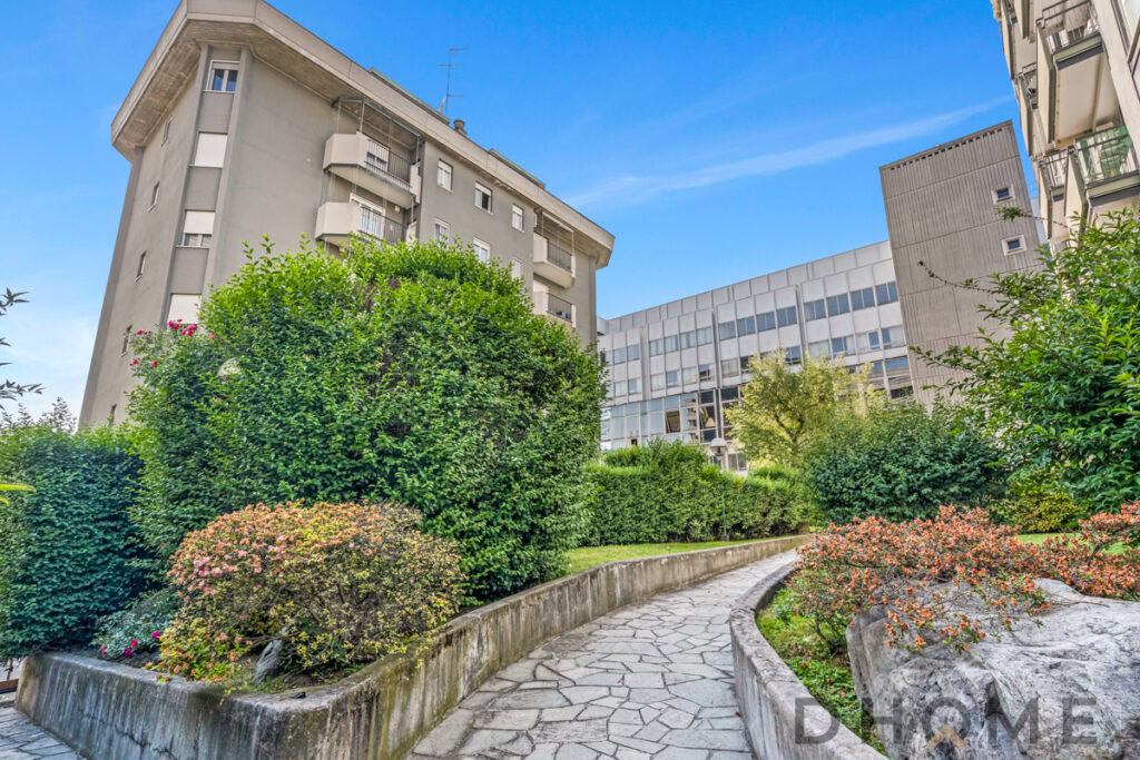 Vicolo alberato nel centro urbano di Milano con grattacieli moderni, verde e giardini curati.