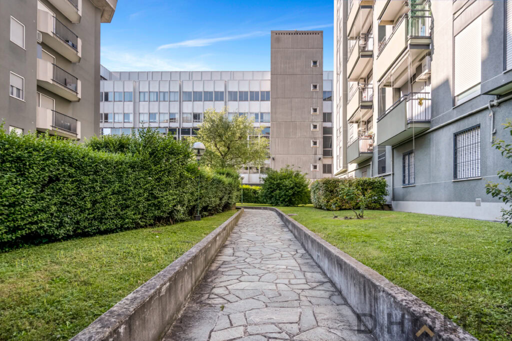 Percorso pavimentato tra giardini e palazzi residenziali a Milano.