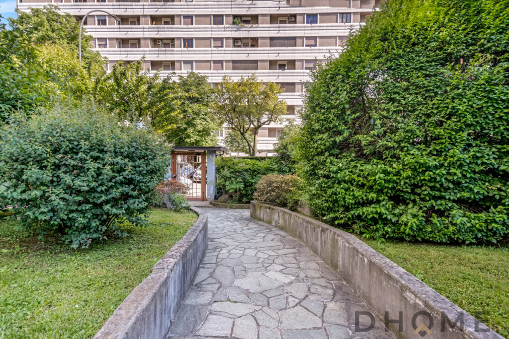 Entrata condominiale con giardino e muro di cinta, zona verde e spazi esterni curati.