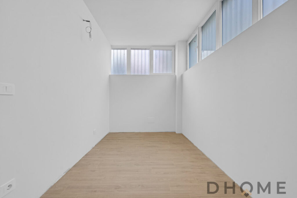 Spazio vuoto in interno con pareti bianche e grandi finestre, ideale per appartamenti moderni.