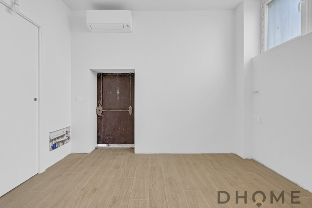 Spazio interno ristrutturato con pavimento in legno e pareti bianche, aria condizionata e finestra luminosa.