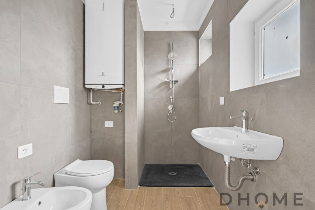 Lavabo, bidet e doccia in bagno moderno con pareti in gres e finestra naturale.