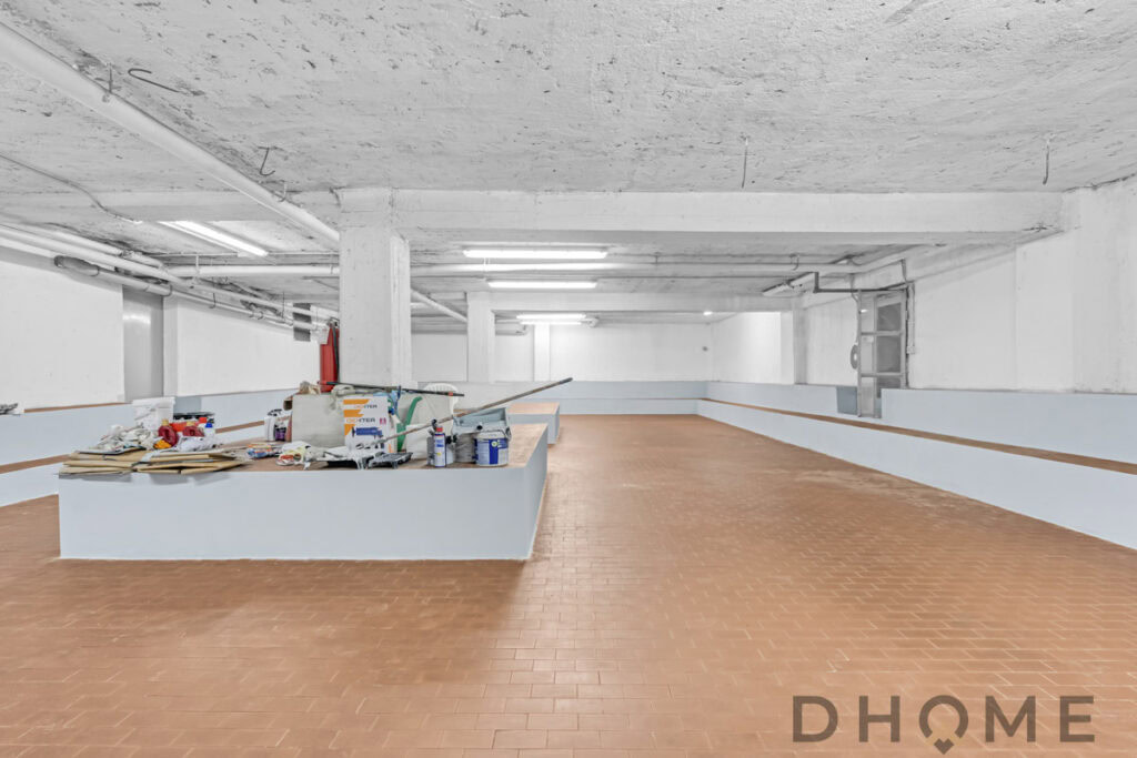 Spazio garage interrato in costruzione, pavimento in piastrelle e strutture in cemento.