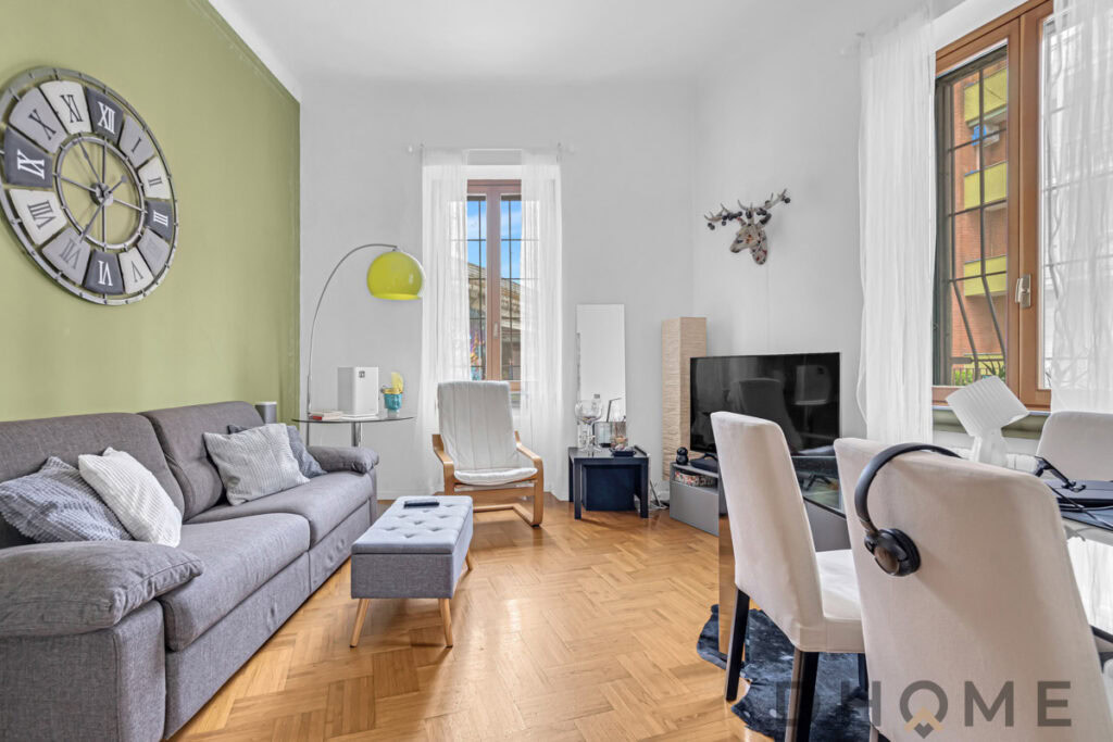 2. Divano grigio con cuscini, soggiorno luminoso con parete verde e grande orologio moderno.