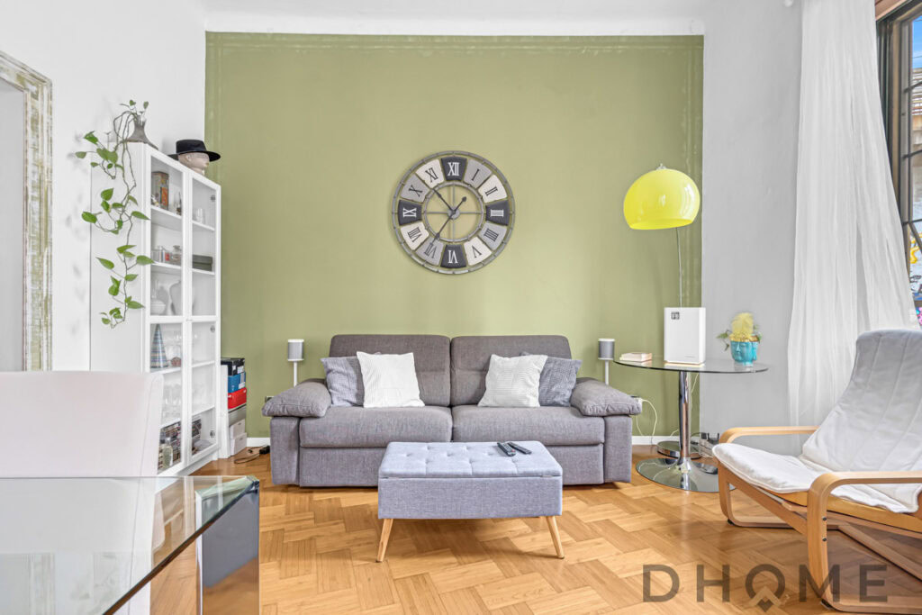 Elegante soggiorno moderno con divano grigio, parete verde e accessori di design.