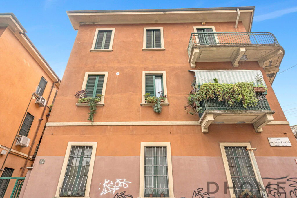 Villetta a schiera con balcone e piante in vasi, stile classico e pietra, facciata arancione, Italia.