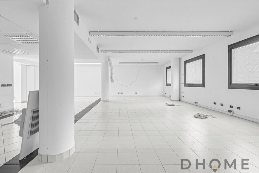 Ampia stanza commerciale in fase di ristrutturazione, pareti bianche e grandi finestre.