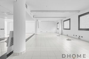 Ampia stanza commerciale in fase di ristrutturazione, pareti bianche e grandi finestre.