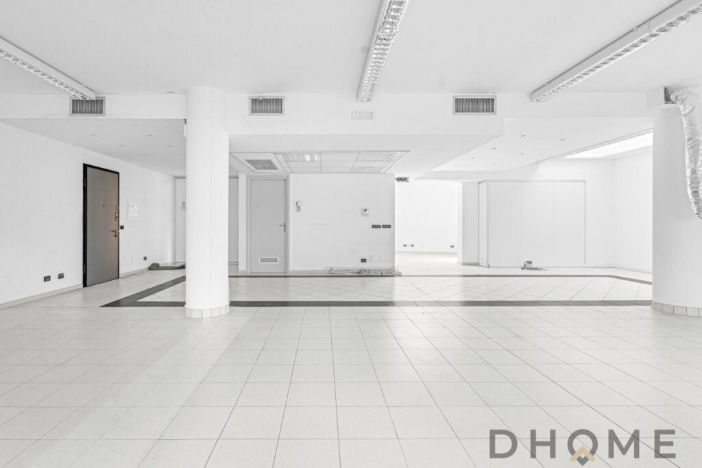 Spazio commerciale vuoto con pavimenti in ceramica e pareti bianche dalla luce naturale.