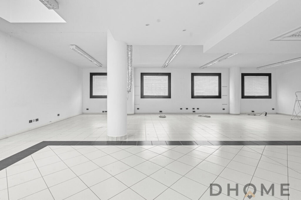 Spazio commerciale vuoto con grandi finestre e illuminazione naturale, ideale per negozi o uffici moderni.