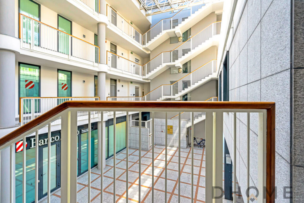 Interno moderno di un condominio con scale e uffici commerciali al piano terra. Design luminoso e funzionale di spazi residenziali e commerciali.