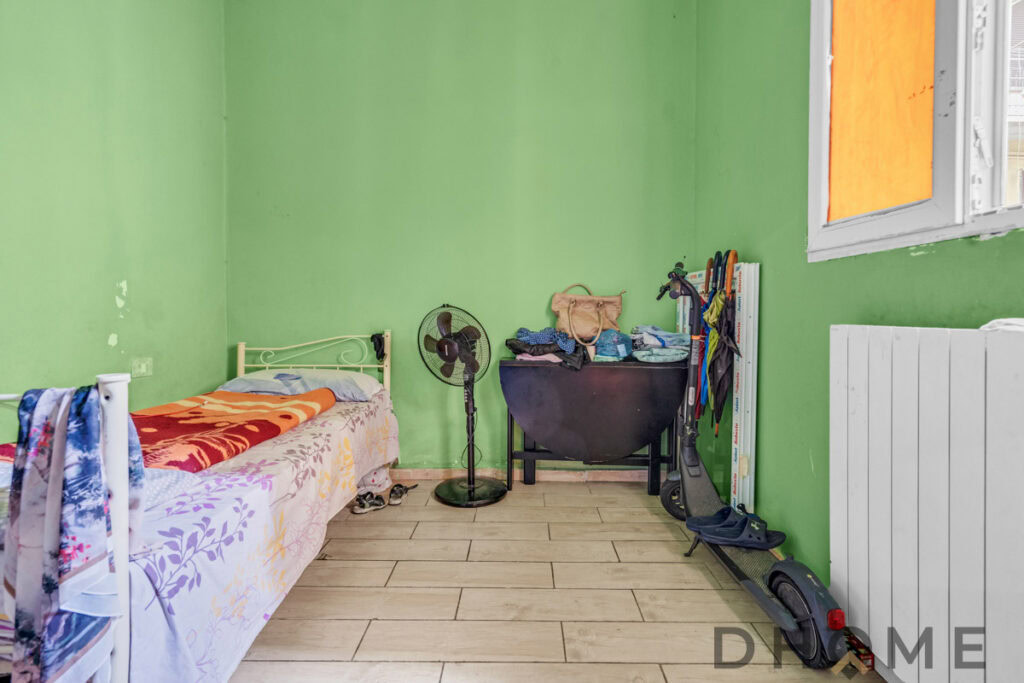 Letto singolo con coperta arancione in una stanza con pareti verdi.