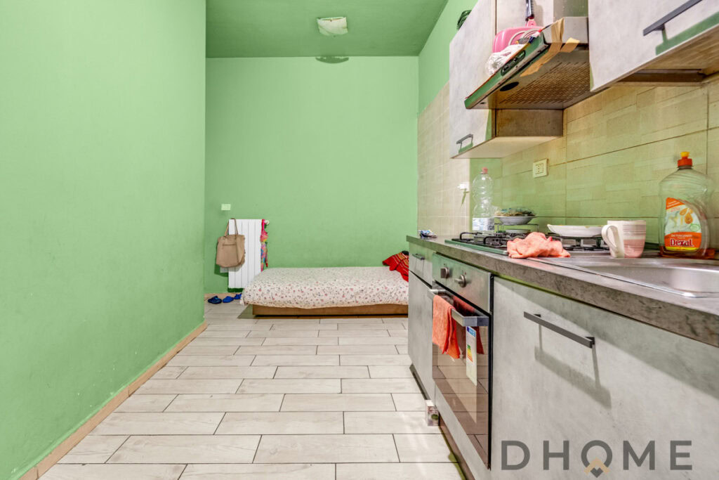 Camera da letto con cucina open space, pareti verdi e arredo semplice. Spazio funzionale e accogliente, ideale per vivere in serenità.