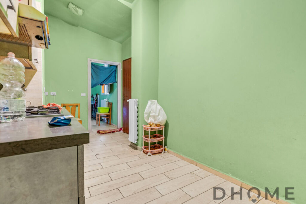 Verde cucina con pareti in lime, mobili e oggetti domestici, vista verso una stanza con tende blu.