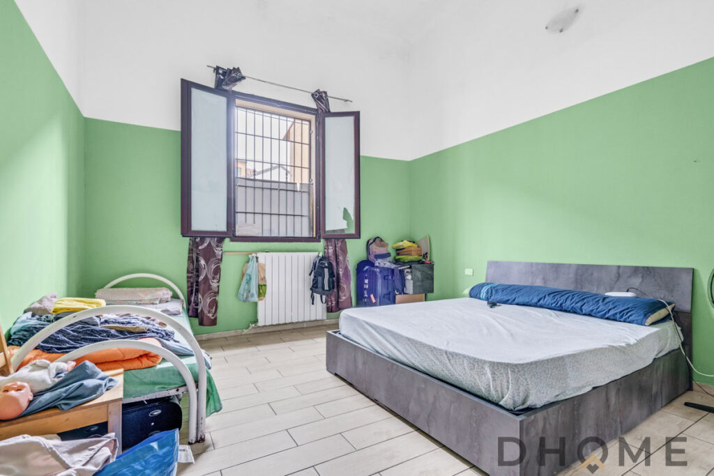 Camera da letto con pareti verde chiaro, finestra aperta, letti e vestiti disordinati, ambiente abitabile e naturale.