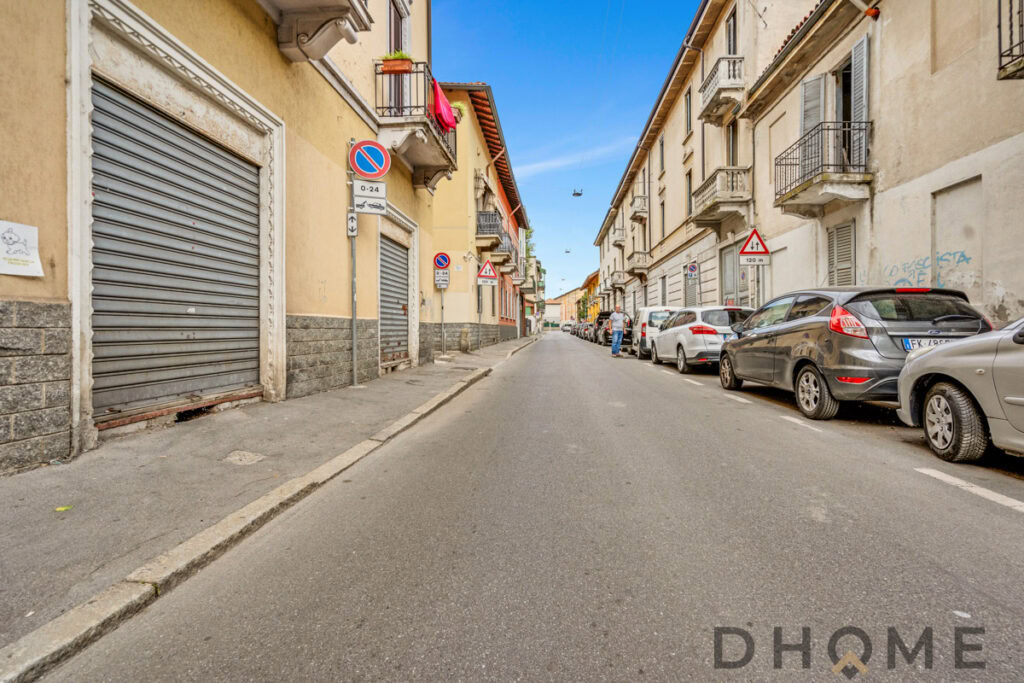 Auto parcheggiate lungo strada in zona urbana, edifici storici e segnaletica stradale visibile.