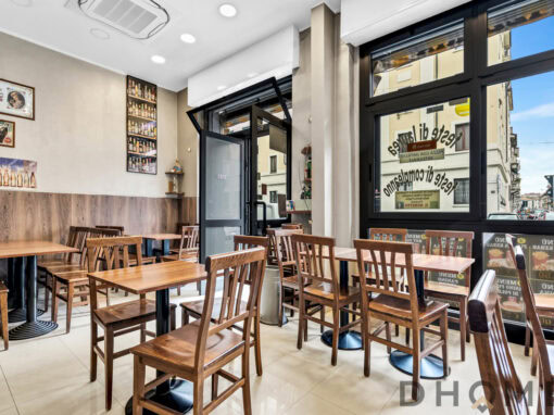 Ampia sala da pranzo in stile moderno con tavoli in legno e sedie in teak, decorata con poster vintage e bottiglie d'arte.