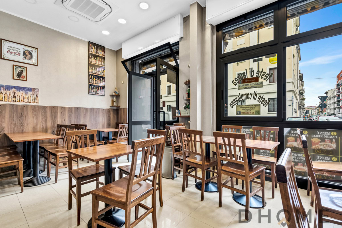 1 Ampia sala da pranzo in stile moderno con tavoli in legno e sedie in teak, decorata con poster vintage e bottiglie d'arte.