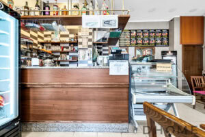 Bancone del bar con espositori e menu, arredamento caldo in legno, atmosfera accogliente, ideale per locali pubblici.