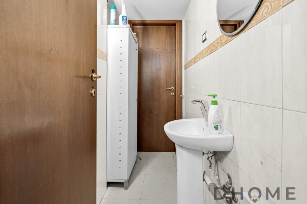Lavandino in bagno con porta in legno, prodotti per l'igiene e mobiletto bianco, design funzionale e pratico.