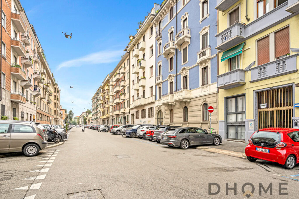 Viale di palazzi residenziali con auto parcheggiate e edifici storici, cielo sereno, prospettiva urbana.