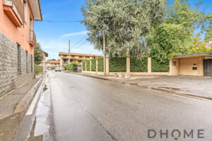 Vicolo residenziale con case e alberi, strada asciutta e cielo sereno.