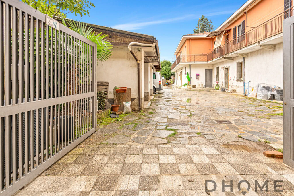 Ingresso esterno di una proprietà residenziale con cortile pavimentato e case in stile italiano.