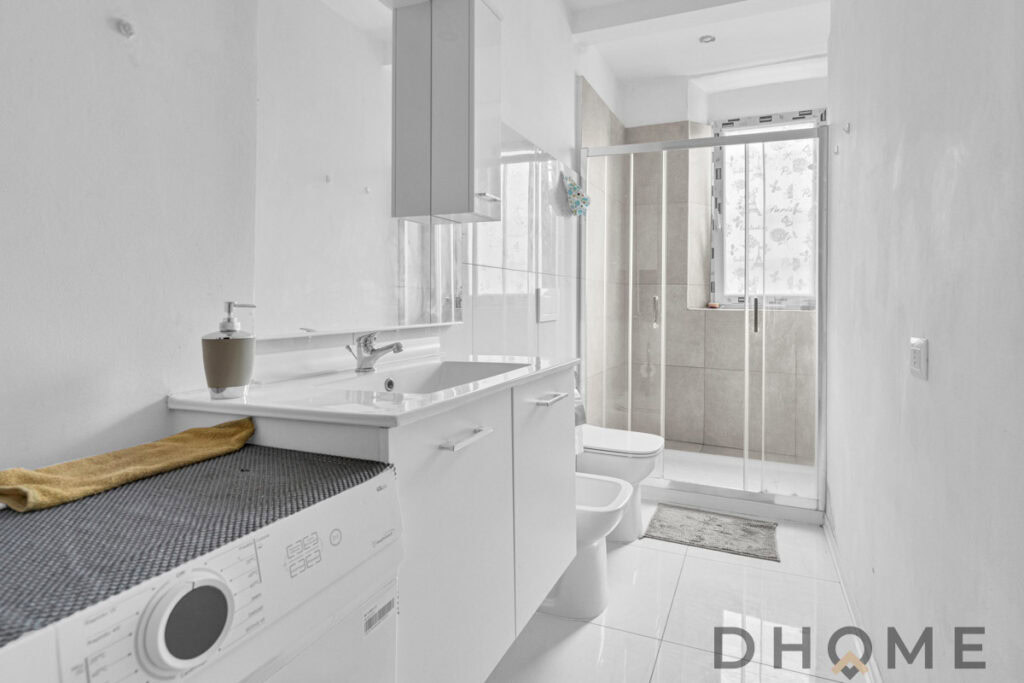 Lavabo bianco con mobile bagno e lavatrice in bagno, spazio moderno e funzionale.