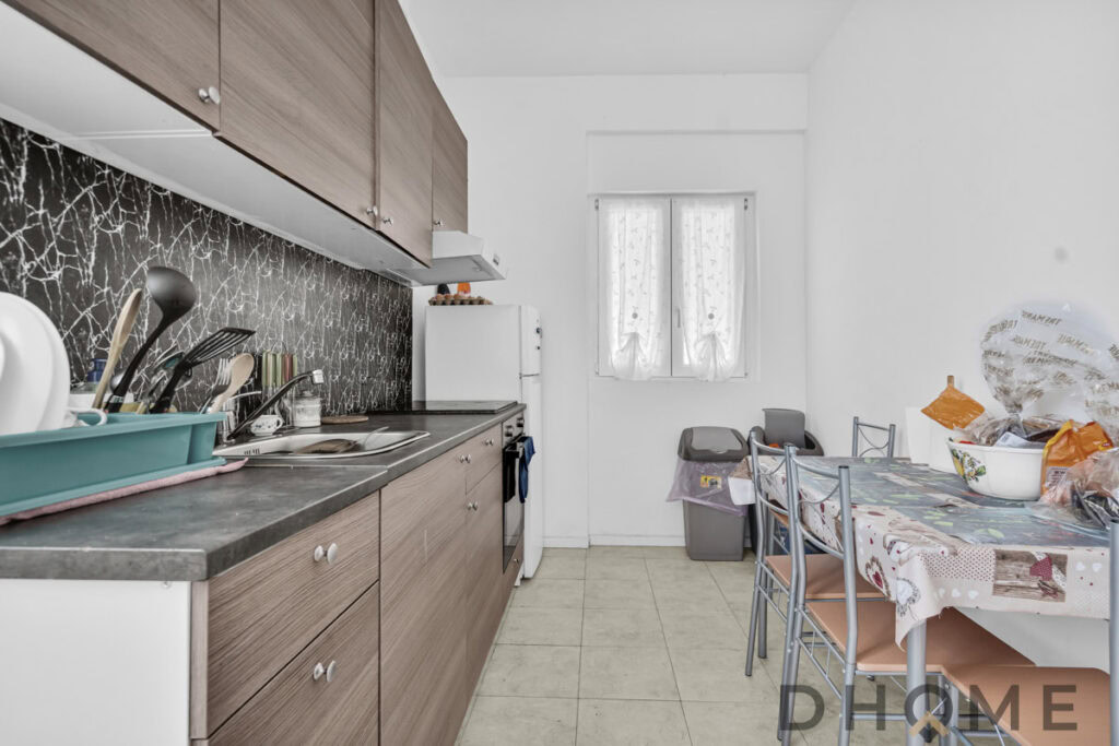 Cucina moderna con mobili in legno chiaro e piano in pietra scura, dotata di elettrodomestici e spazio pranzo.