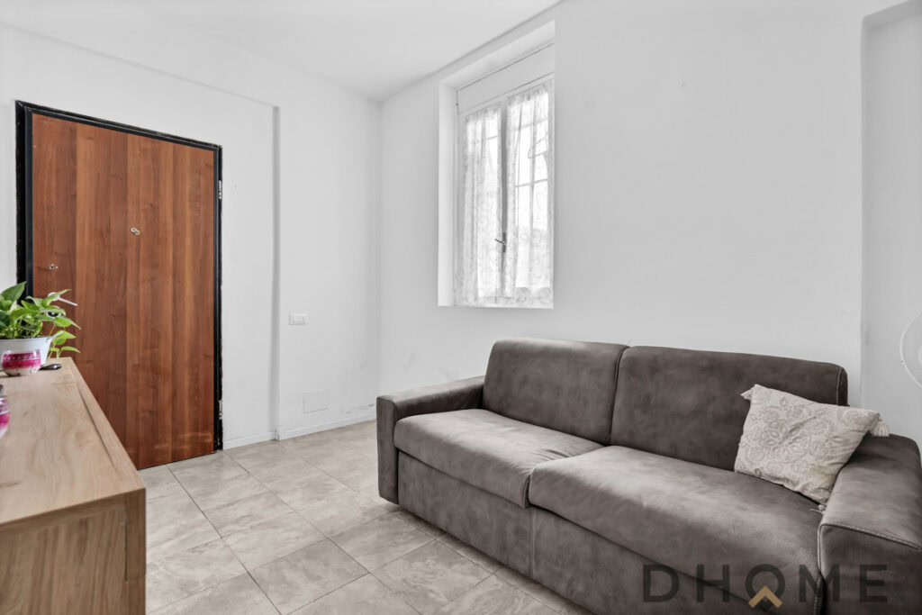 Divano grigio elegante in soggiorno con pareti bianche e finestra illuminata.