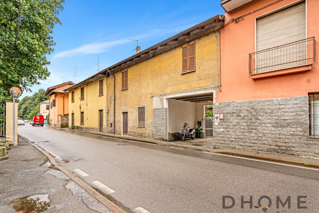 Casolare storico colorato con garage e scooter in strada di paese, vista tranquilla e vicinanze servizi.