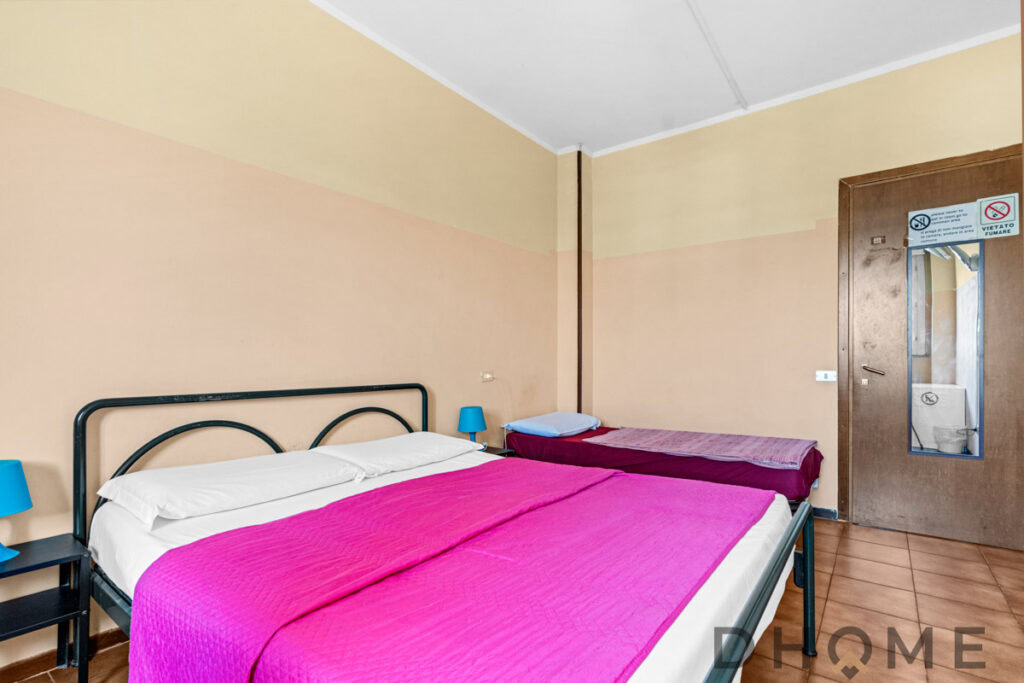 Letto matrimoniale con lenzuola bianche e coperta rosa, in camera semplice e accogliente.