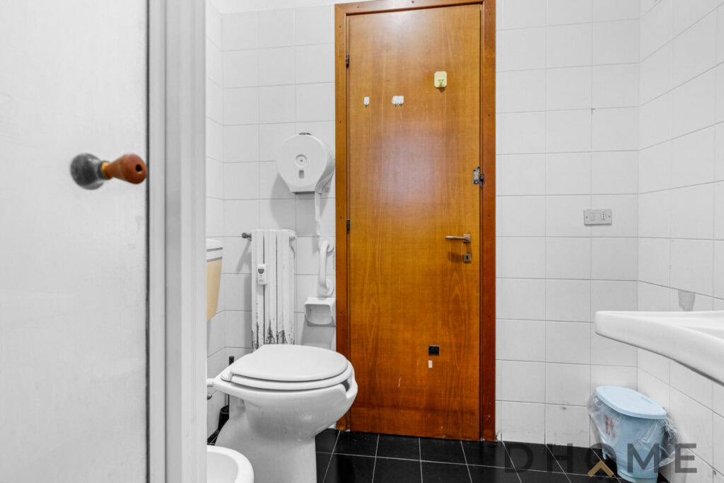 Lavabo e servizi igienici in bagno di ufficio o abitazione con rivestimenti in ceramica bianca.