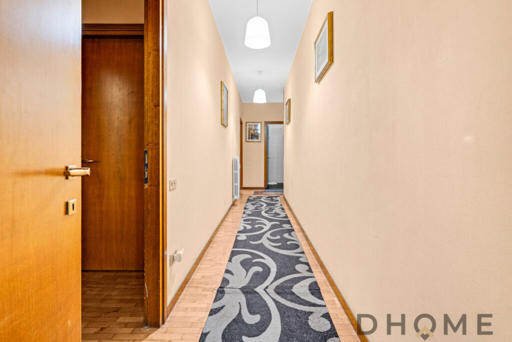 Corridor of an apartment with wooden doors, beige walls and decorative rug.