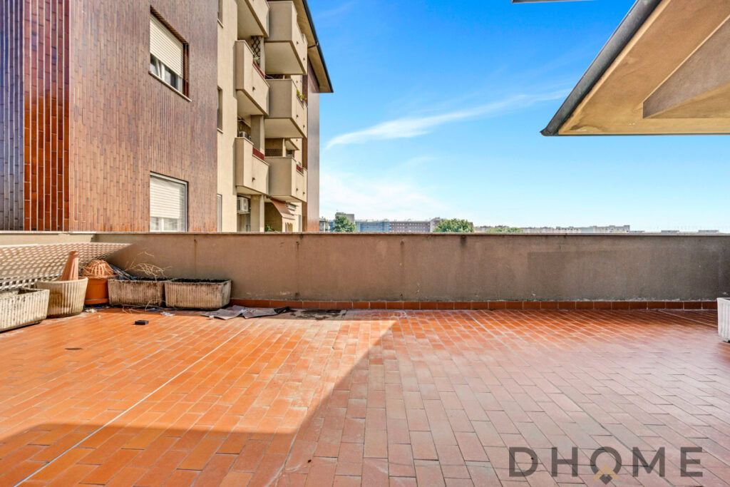 Balcone di città con pavimento in cotto e vista su edifici e cielo azzurro.