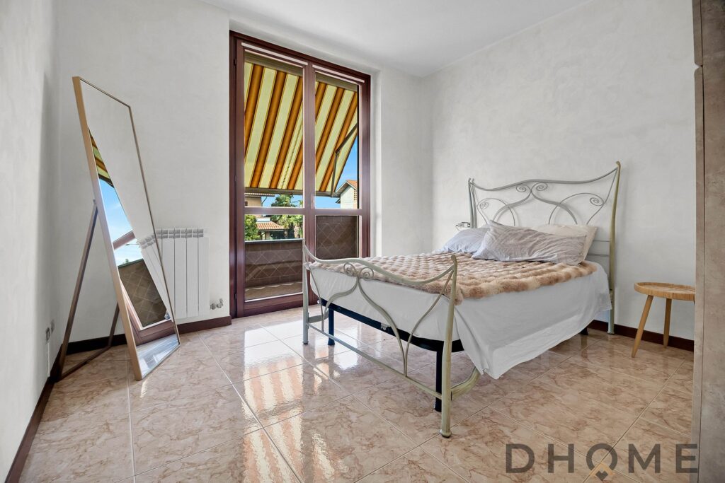 Letto matrimoniale con stile romantico e dettagli in ferro battuto, illuminato dalla luce naturale della finestra.