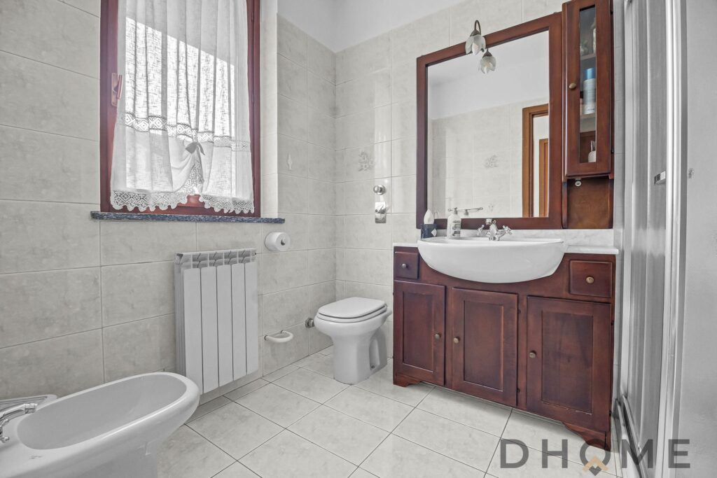 Lavabo in stile classico con mobile in legno e grande specchio finestra con tende ricamate.