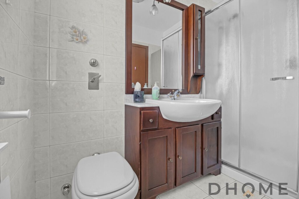 Specchio bagno con mobili in stile classico in legno scuro, lavabo e accessori moderni.