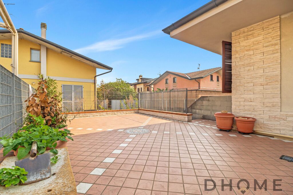 Balcone di casa con piastrelle in terracotta e piante in vaso, vista su edificio residenziale, spazio esterno accogliente.