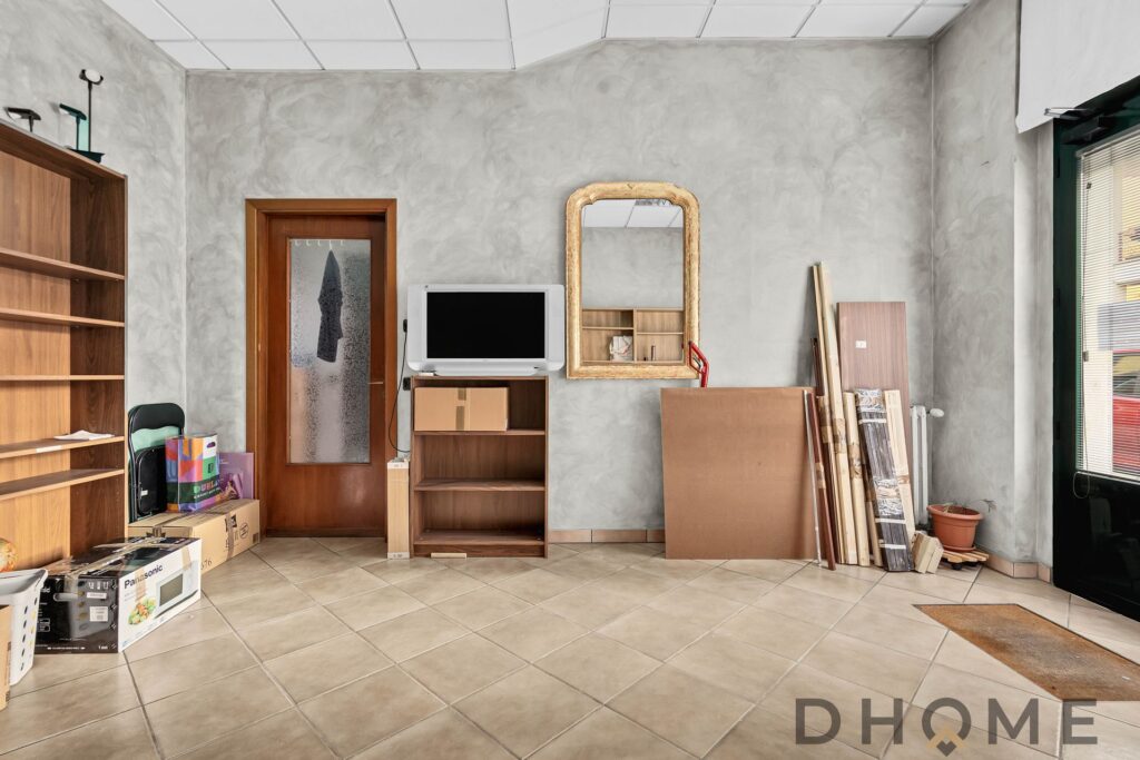 Mobile da soggiorno in medie condizioni, con televisore, libri e oggetti vari, pareti grigie e pavimenti in gres porcellanato..