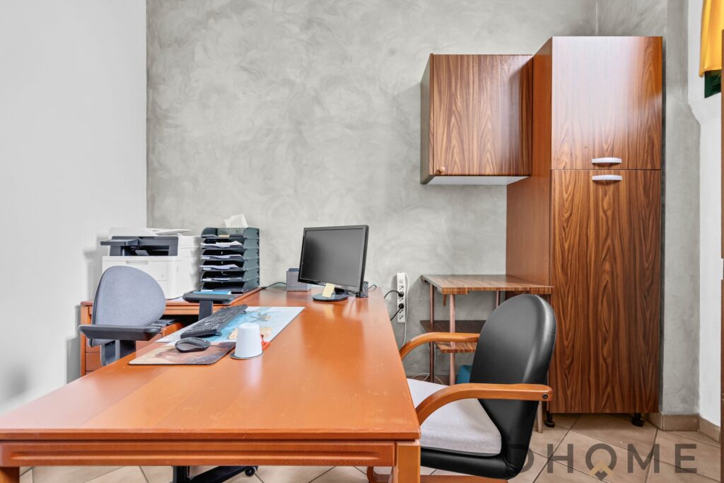 Scrivania per ufficio con arredi in legno, computer e stampante, ambiente lavorativo professionale.