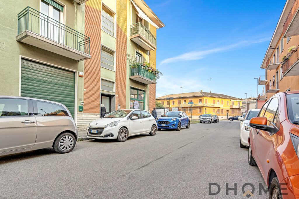 Auto parcheggiata davanti a un edificio residenziale a Milano, con palazzi colorati e un cielo sereno.
