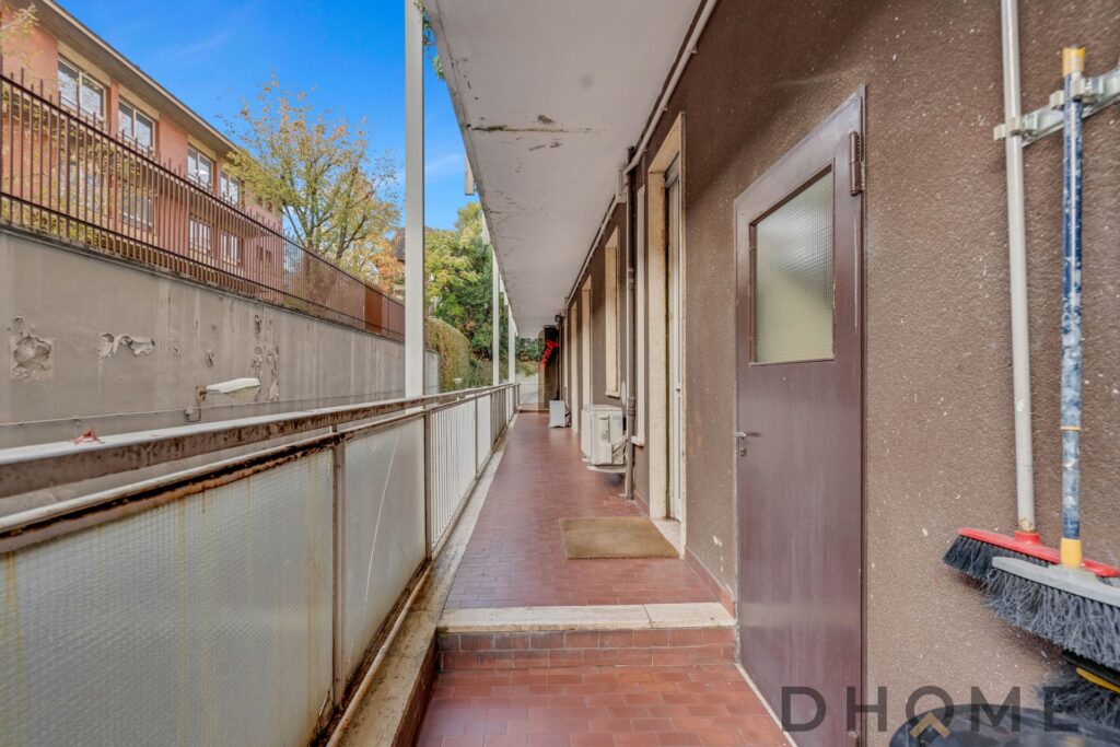 Balcone di appartamento con pavimento in piastrelle e porte in legno, spazio esterno residenziale.
