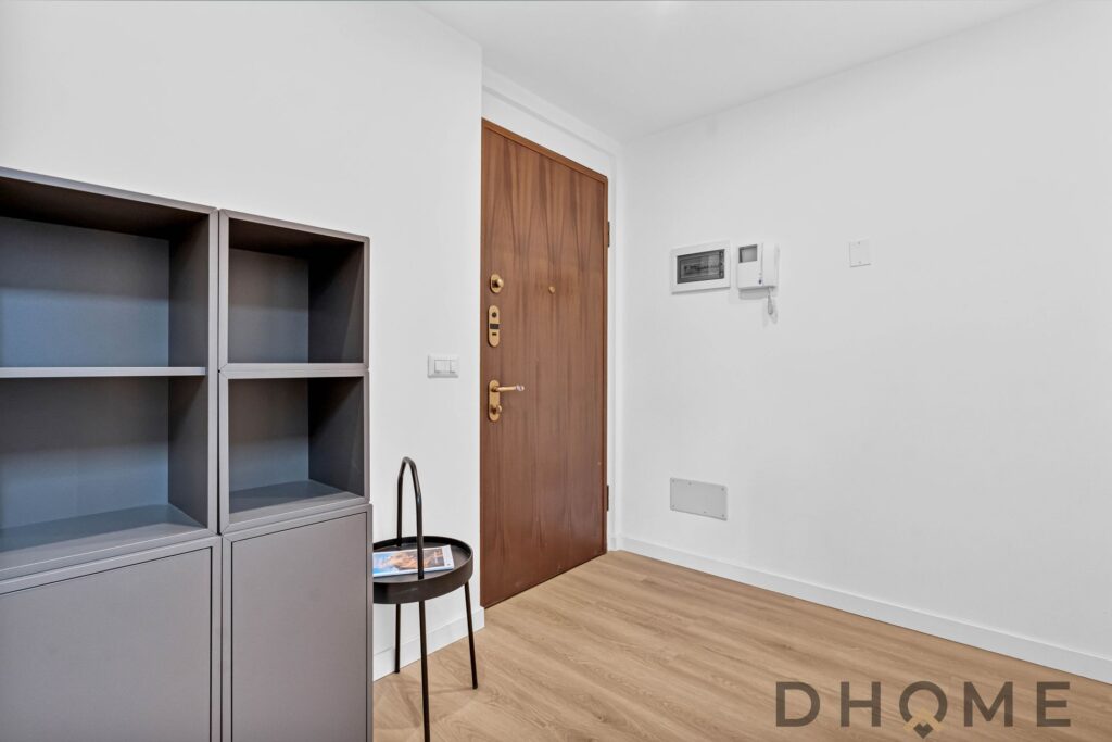 Armadio grigio con cubi vuoti e porta ingresso in legno. Interno moderno, pareti bianche e pavimento in parquet chiaro.