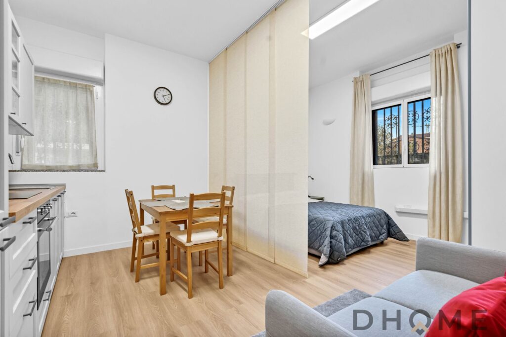 Soggiorno con cucina a vista e camera da letto separata, arredamento moderno e luminoso.