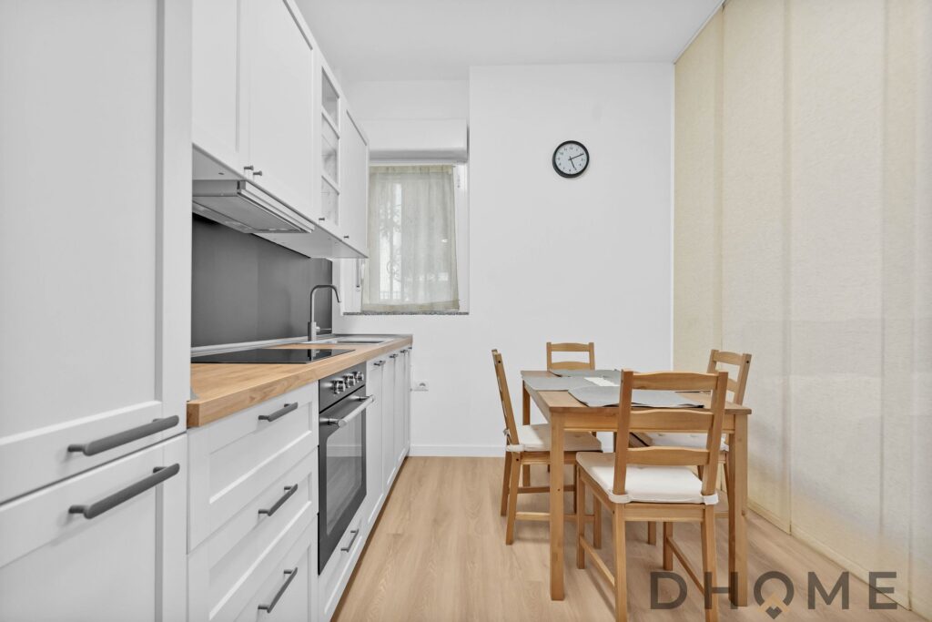 Cucina moderna bianca con zona pranzo in legno, luce naturale, stile minimal e funzionale, ideale per arredo di casa DHOME.